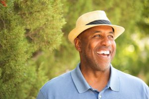 Man with hat, cheerfully laughing in the outdoors - represents man who has relied on Christ to overcome sin