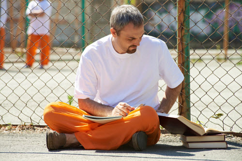 Prisoner with orange and white clothes reading in jail yard