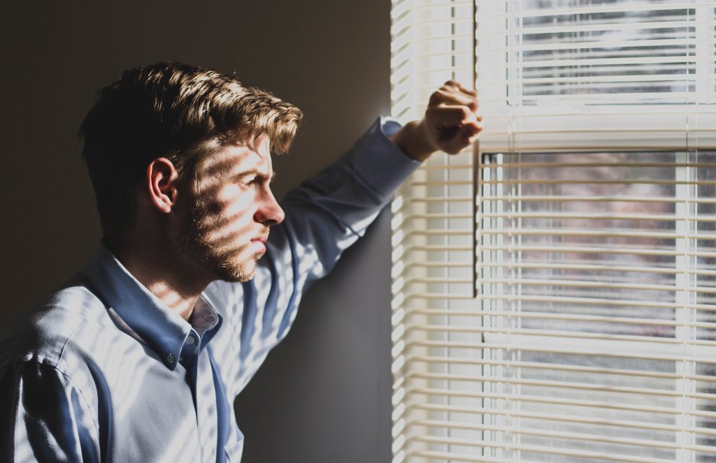 Man looking through window blinds