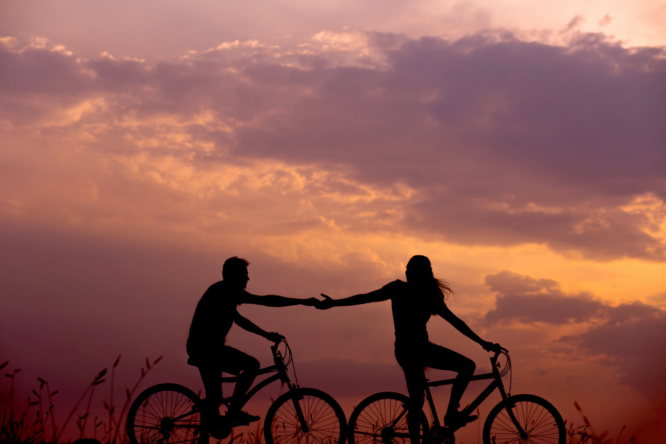 Man and woman silhouette on bicycles in front of orange sky
