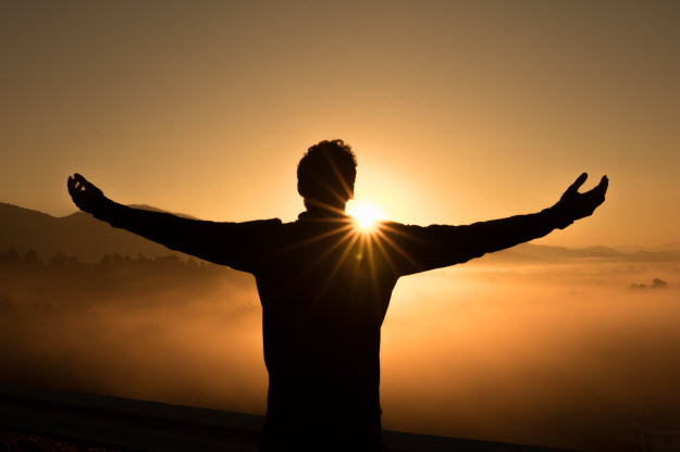 man with arms extended with joy, welcoming a rising sun
