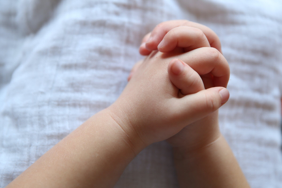 Child's hands clasped in prayer, resting on a white blanket