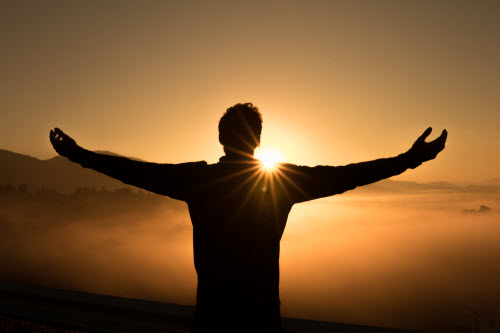 Man standing in rising sun with arms extended