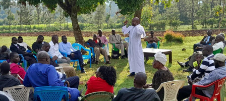 Pastor Oguta teaching in a field sorrounded by people 