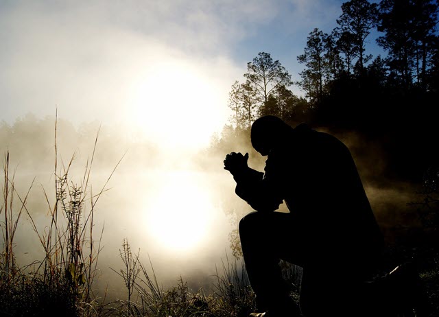 Man praying by pond in early morning light