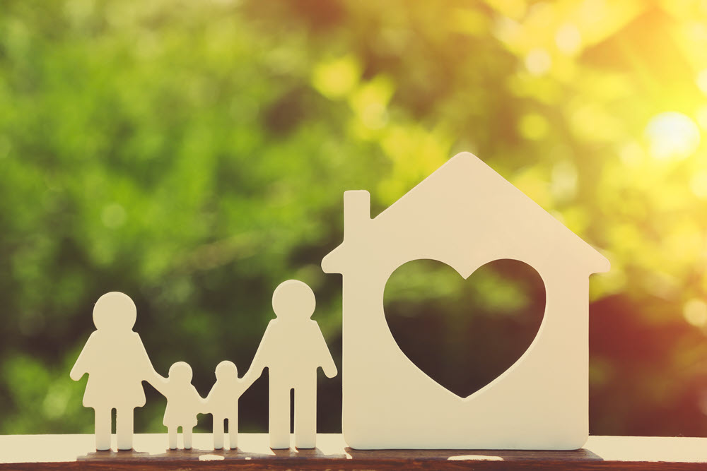 Family holding hands by wooden home with heart on it